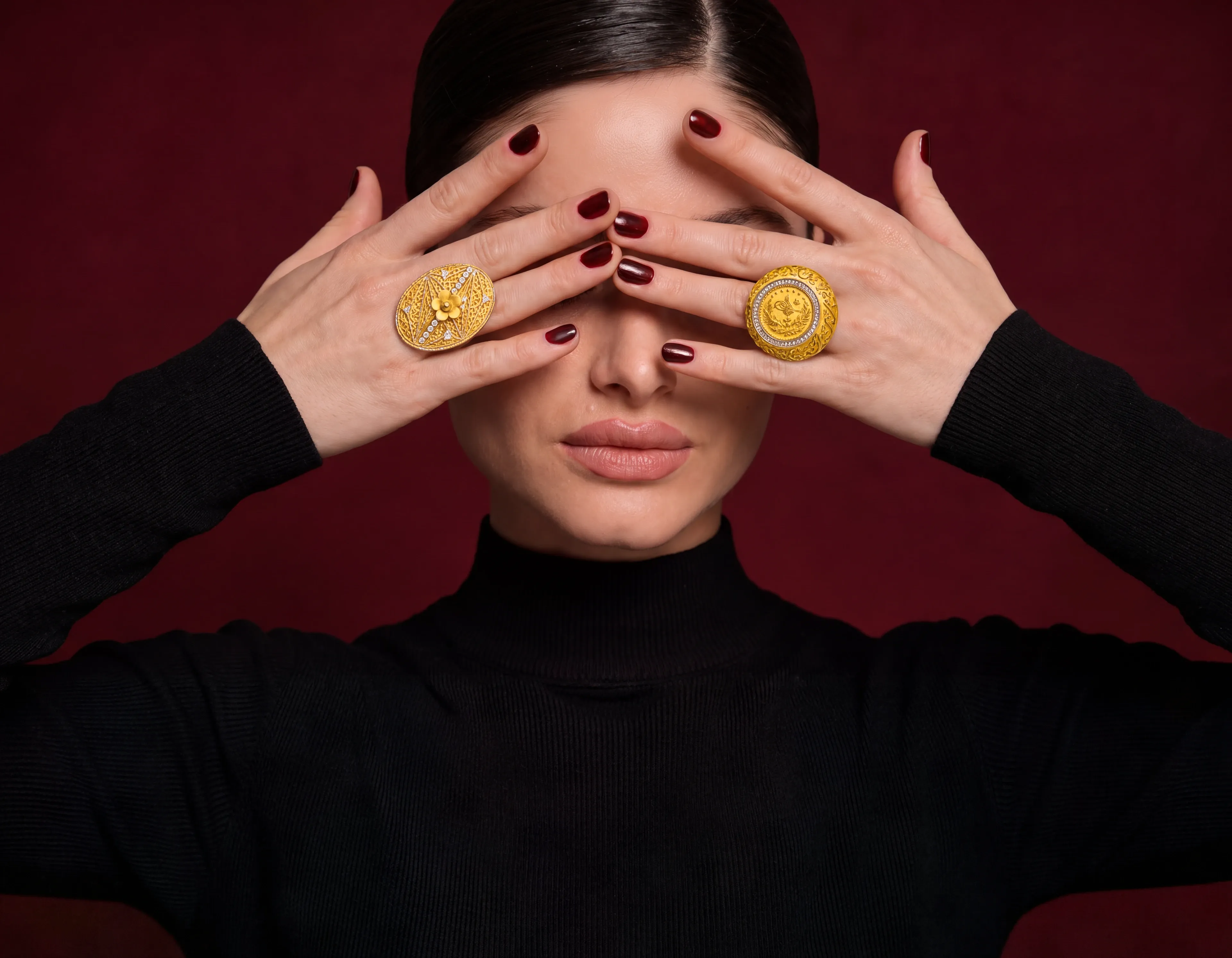 A model with both hands over her eyes, wearing the Floral Basket Ring and the Rashadi Coin Statement Ring in 21K gold